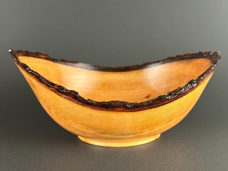 Golden live-edge bowl. Golden wooden bowl with a thin dark bark edge and raised sides.