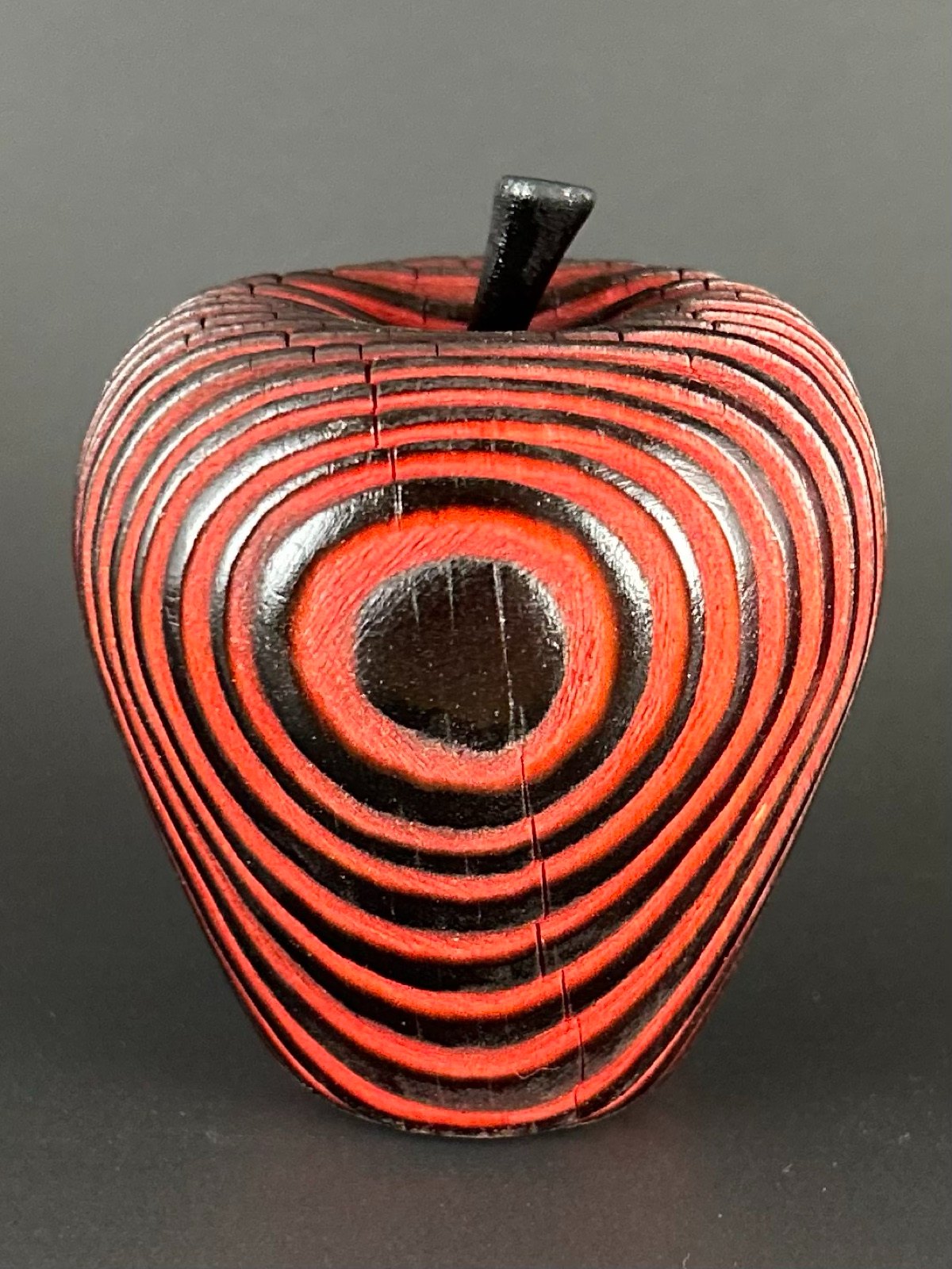 Red apple form. Red apple-shaped object with dark concentric grooves and a small stem.