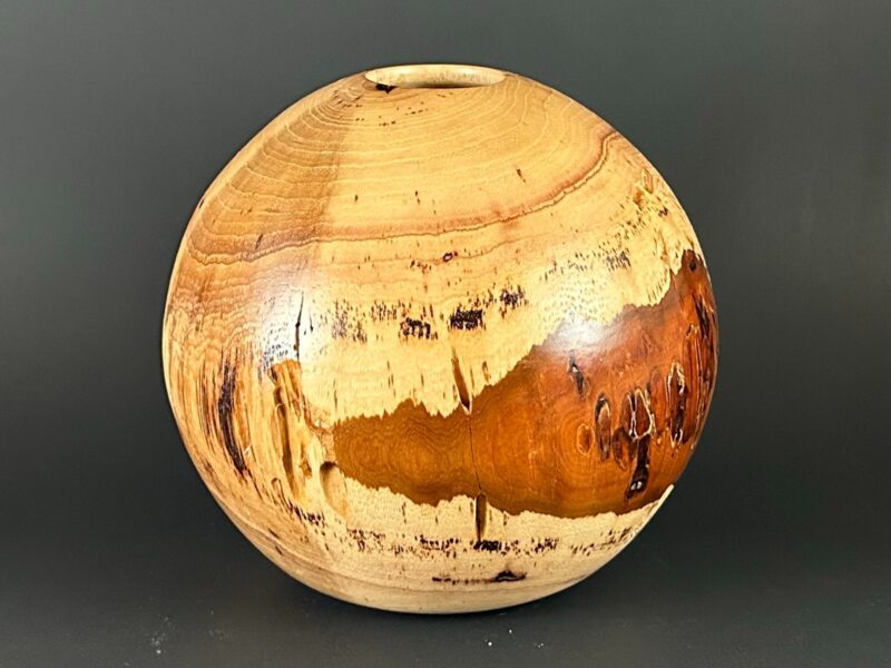 Rounded hollow vessel. Rounded wooden vessel with a small opening and cream and amber grain.