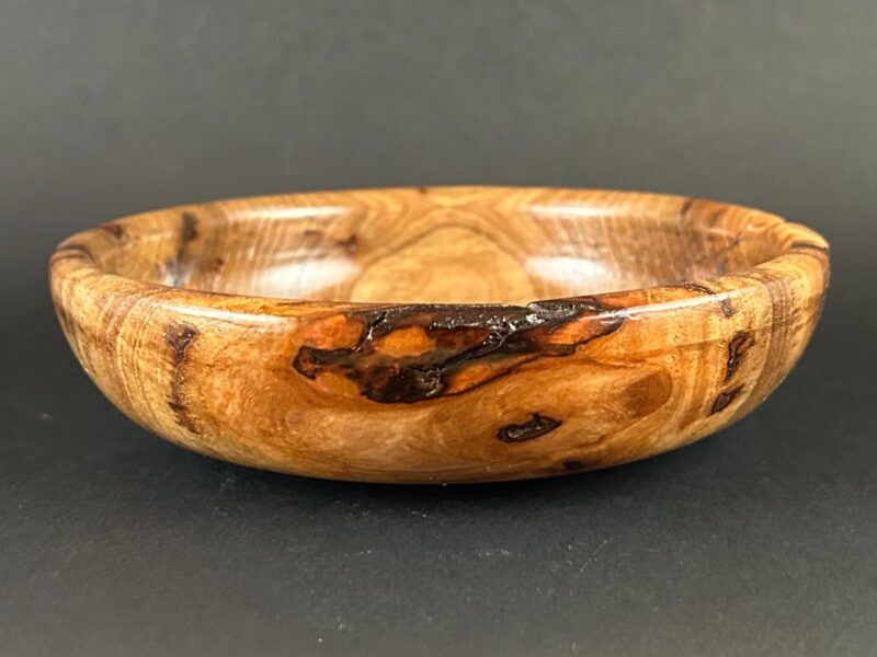 Low knotted bowl. Low wooden bowl with a dark knot interrupting golden and brown grain.