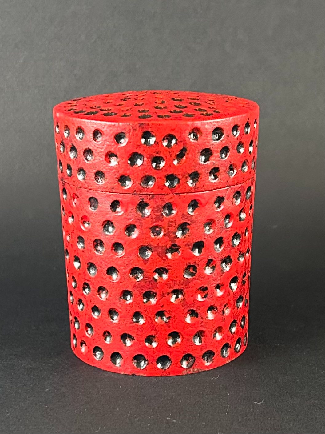 Red pierced box. Red cylindrical wooden box with rows of circular openings.