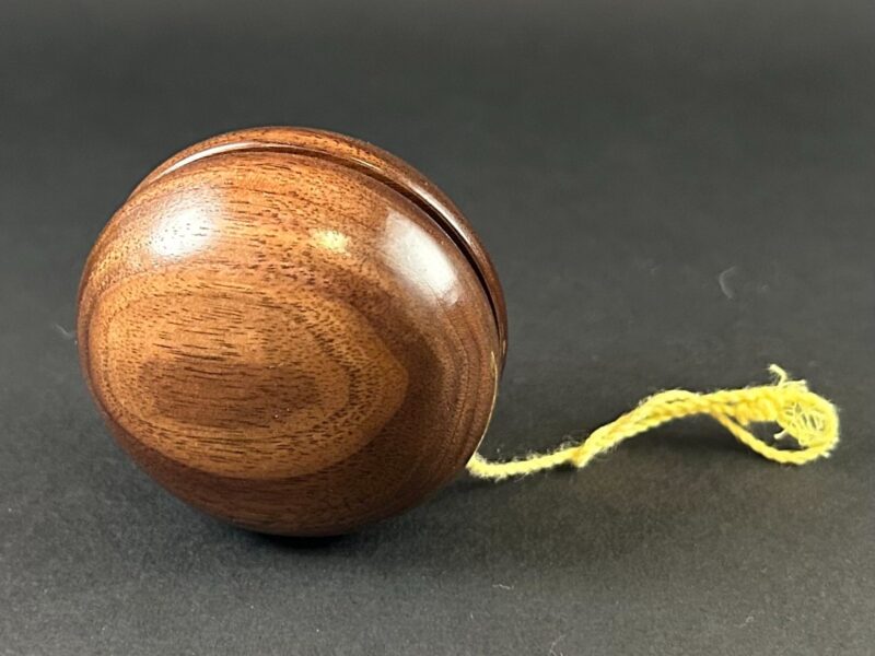 Wooden yo-yo. Round wooden yo-yo with a yellow string beside it.