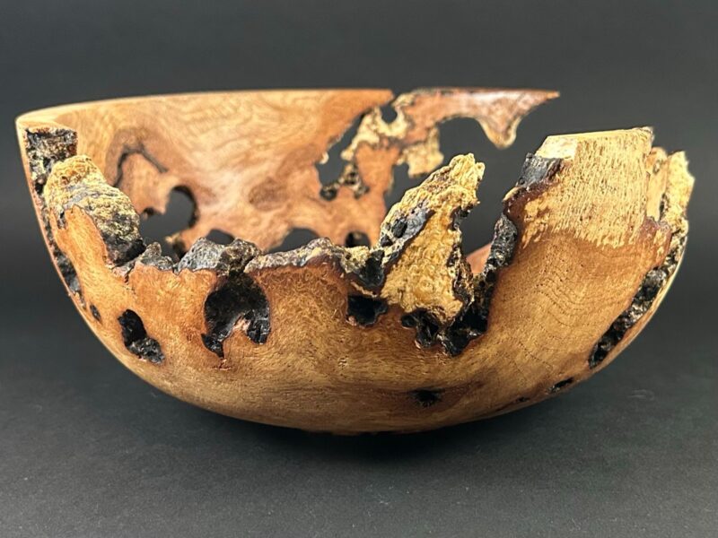 Sculptural bowl. Wooden bowl with irregular dark openings and a textured, uneven edge.