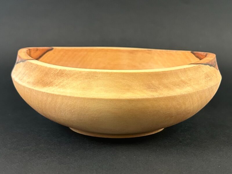 Low-profile bowl. Low pale wooden bowl with a wide rim and contrasting dark patches.